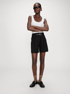 Person wearing a white tank top, black shorts, and black shoes on a white background